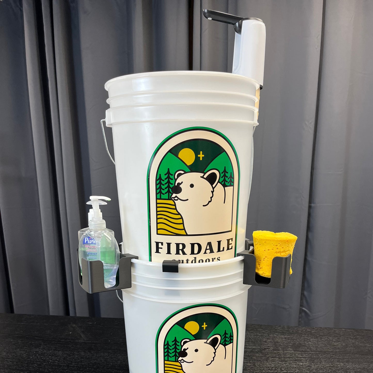 Two stacked buckets with a water pump and soap holders attached